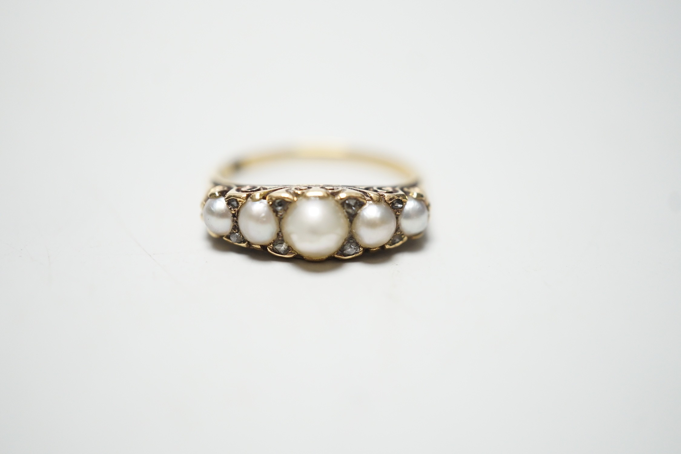 A late Victorian yellow metal (stamped 18) and five stone graduated split pearl set half hoop ring, with diamond chip spacers, size O, gross weight 2.8 grams.